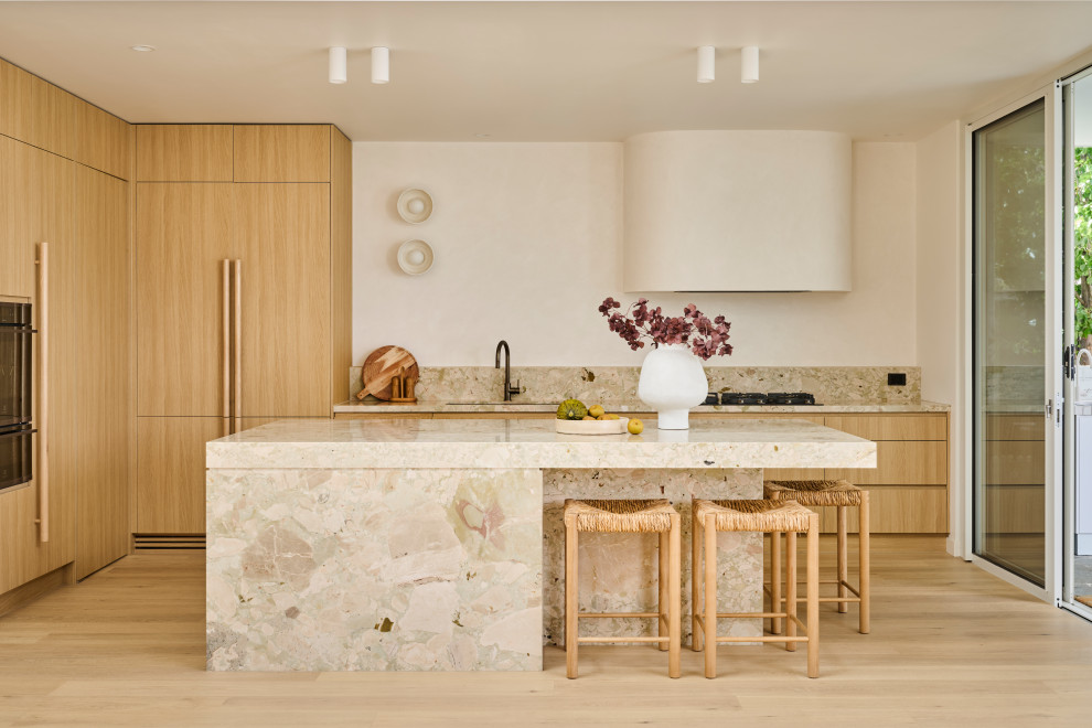 Inspiration for a mid-sized contemporary l-shaped open plan kitchen in Geelong with an undermount sink, flat-panel cabinets, light wood cabinets, marble benchtops, light hardwood floors, with island, beige splashback, stone slab splashback, panelled appliances, beige floor and beige benchtop.