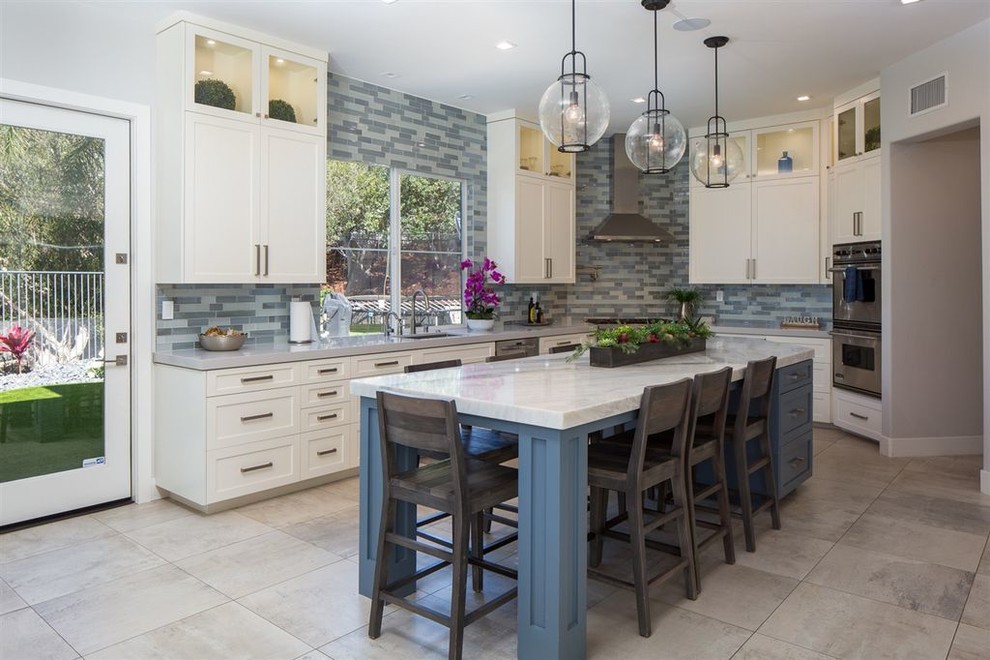 This is an example of a large contemporary u-shaped open plan kitchen in San Diego with shaker cabinets, white cabinets, quartzite benchtops, blue splashback, glass tile splashback, stainless steel appliances, porcelain floors, with island, grey floor and white benchtop.