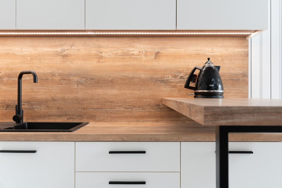 Inspiration for a mid-sized modern l-shaped open plan kitchen in Sydney with white cabinets, wood benchtops, timber splashback, with island, brown benchtop, a single-bowl sink, black appliances, flat-panel cabinets, brown splashback, porcelain floors and white floor.
