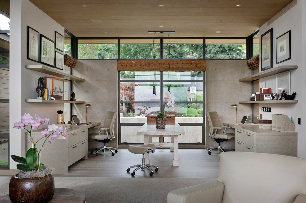 This is an example of a contemporary home office in Seattle with white walls, a built-in desk and beige floor.