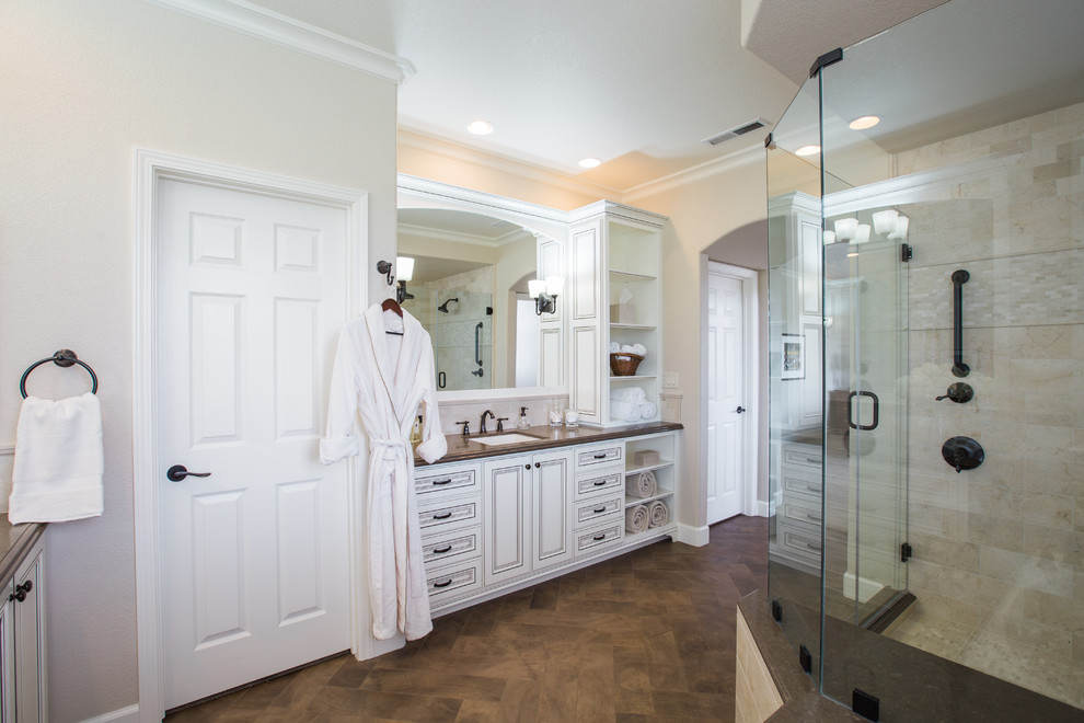 Photo of a large traditional master bathroom in San Francisco with furniture-like cabinets, distressed cabinets, an undermount tub, a corner shower, a one-piece toilet, beige tile, stone tile, beige walls, porcelain floors, an undermount sink, engineered quartz benchtops, brown floor and a hinged shower door.