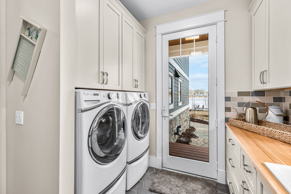 Large arts and crafts galley utility room in Detroit with a drop-in sink, shaker cabinets, white cabinets, wood benchtops, multi-coloured splashback, glass tile splashback, beige walls, porcelain floors, a side-by-side washer and dryer, grey floor and brown benchtop.