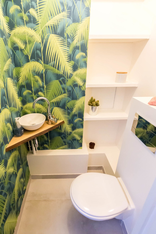 This is an example of a small modern powder room in Paris with open cabinets, white cabinets, a wall-mount toilet, multi-coloured walls, a console sink, beige floor, brown benchtops, wood benchtops and ceramic floors.