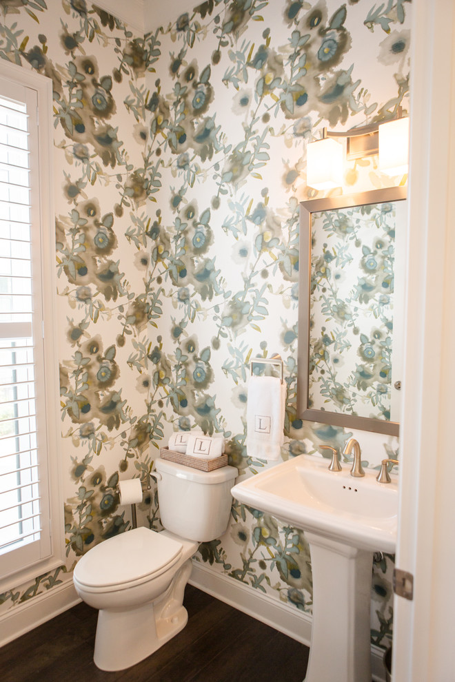 This is an example of a mid-sized traditional powder room in Atlanta with a two-piece toilet, multi-coloured walls, dark hardwood floors, a pedestal sink and brown floor.