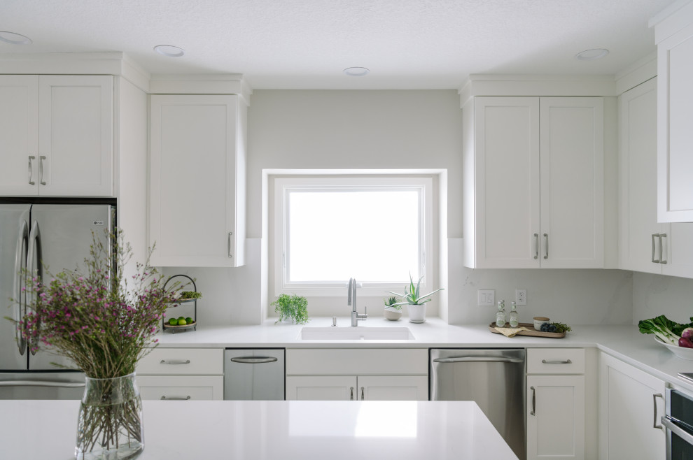 Large transitional l-shaped laminate floor and brown floor eat-in kitchen photo with an undermount sink, shaker cabinets, white cabinets, quartz countertops, white backsplash, quartz backsplash, stainless steel appliances, an island and white countertops