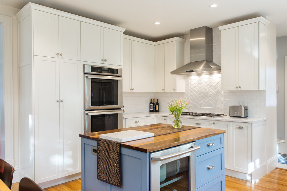 This is an example of a mid-sized traditional u-shaped eat-in kitchen in Boston with an undermount sink, shaker cabinets, white cabinets, marble benchtops, white splashback, subway tile splashback, stainless steel appliances, light hardwood floors and with island.