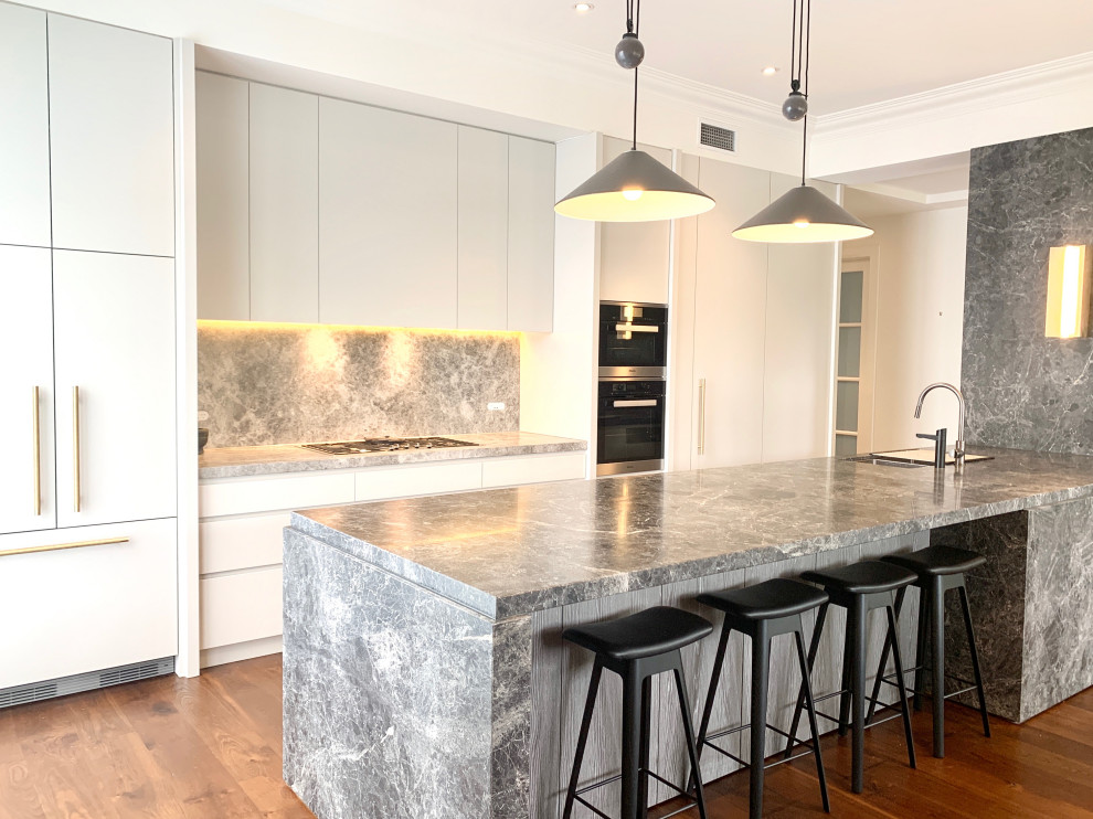 Inspiration for a large traditional galley eat-in kitchen in Melbourne with a drop-in sink, shaker cabinets, grey cabinets, grey splashback, stone slab splashback, black appliances, dark hardwood floors, with island, brown floor and grey benchtop.