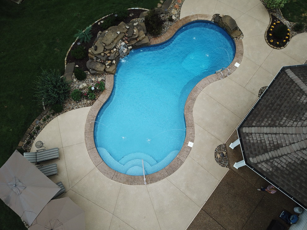 Mid-sized traditional backyard custom-shaped natural pool in St Louis with a water feature and stamped concrete.