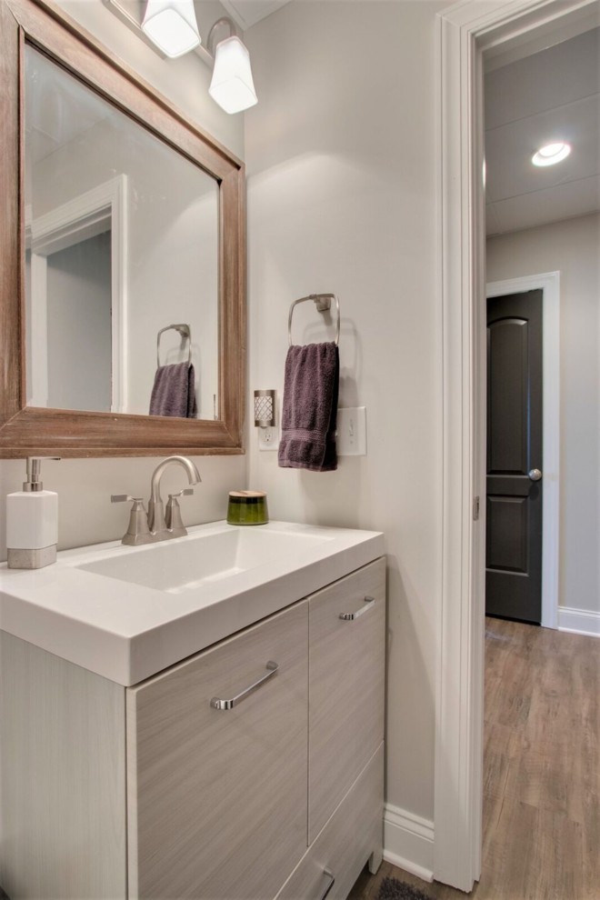 Inspiration for a large transitional powder room in Nashville with flat-panel cabinets, grey cabinets, grey walls, medium hardwood floors, a drop-in sink, brown floor and white benchtops.