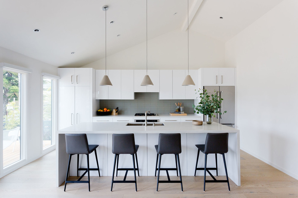 Small contemporary galley eat-in kitchen in Los Angeles with flat-panel cabinets, white cabinets, grey splashback, stainless steel appliances, light hardwood floors, with island, beige floor, an undermount sink, quartz benchtops, glass tile splashback and white benchtop.