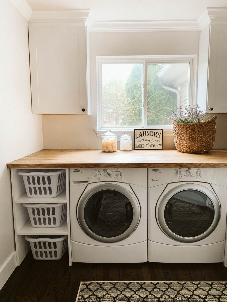 Photo of a mid-sized country utility room in Detroit with shaker cabinets, white cabinets, wood benchtops, white walls, a side-by-side washer and dryer and brown floor.