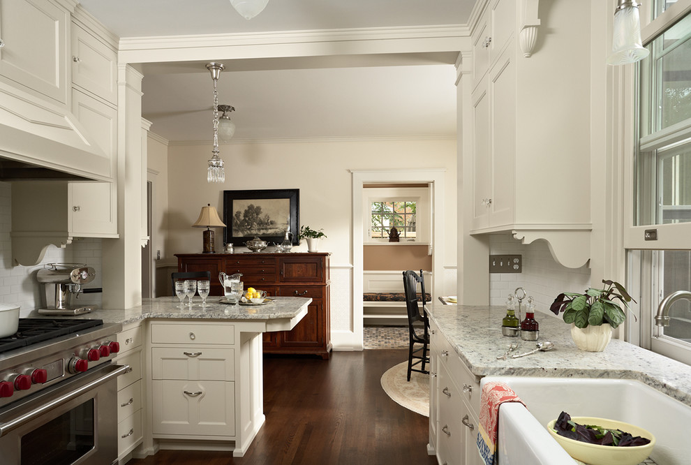 Inspiration for a mid-sized traditional u-shaped eat-in kitchen in Minneapolis with a farmhouse sink, recessed-panel cabinets, white cabinets, granite benchtops, white splashback, ceramic splashback, stainless steel appliances, dark hardwood floors and a peninsula.