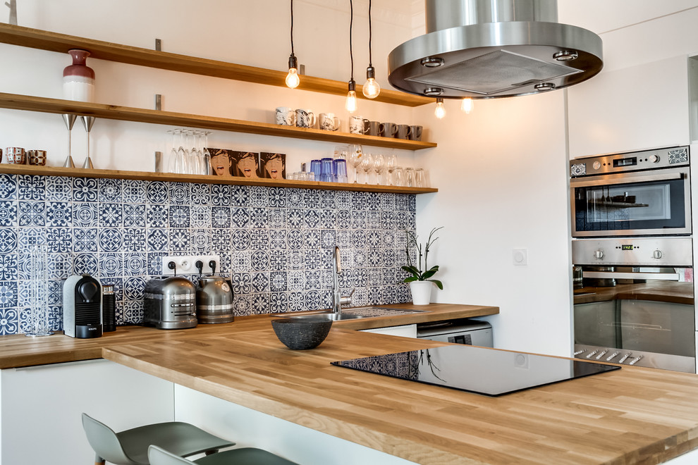 Inspiration for a contemporary u-shaped open plan kitchen in Montreal with a drop-in sink, open cabinets, wood benchtops, multi-coloured splashback, cement tile splashback, stainless steel appliances and a peninsula.