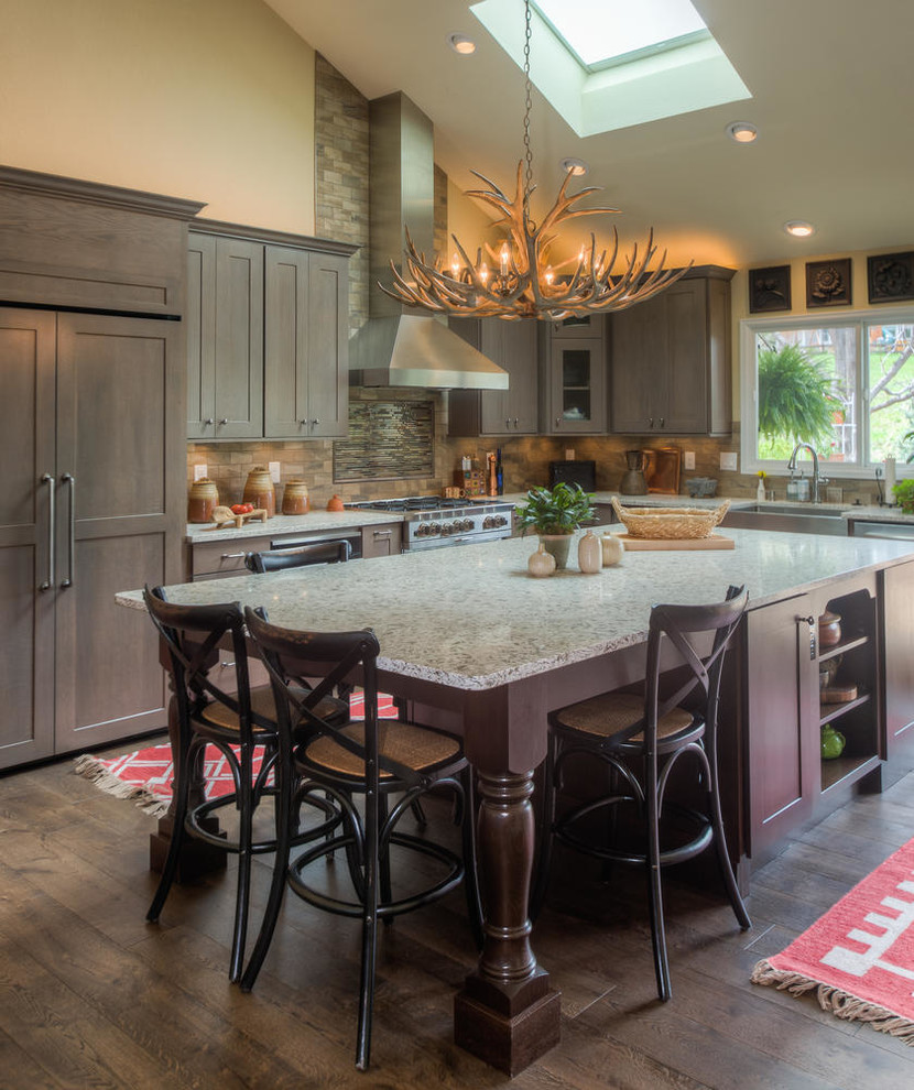 Inspiration for a country l-shaped kitchen in Denver with shaker cabinets, brown cabinets, beige splashback, stainless steel appliances, medium hardwood floors, with island and brown floor.