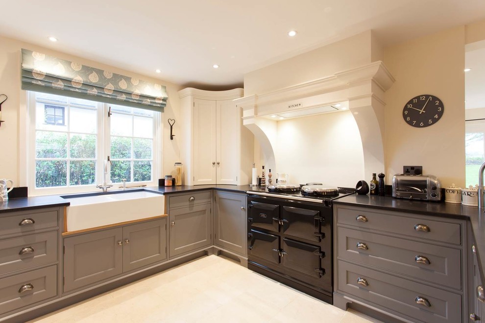 Inspiration for a mid-sized traditional u-shaped eat-in kitchen in Essex with a farmhouse sink, grey cabinets, granite benchtops, black appliances and limestone floors.