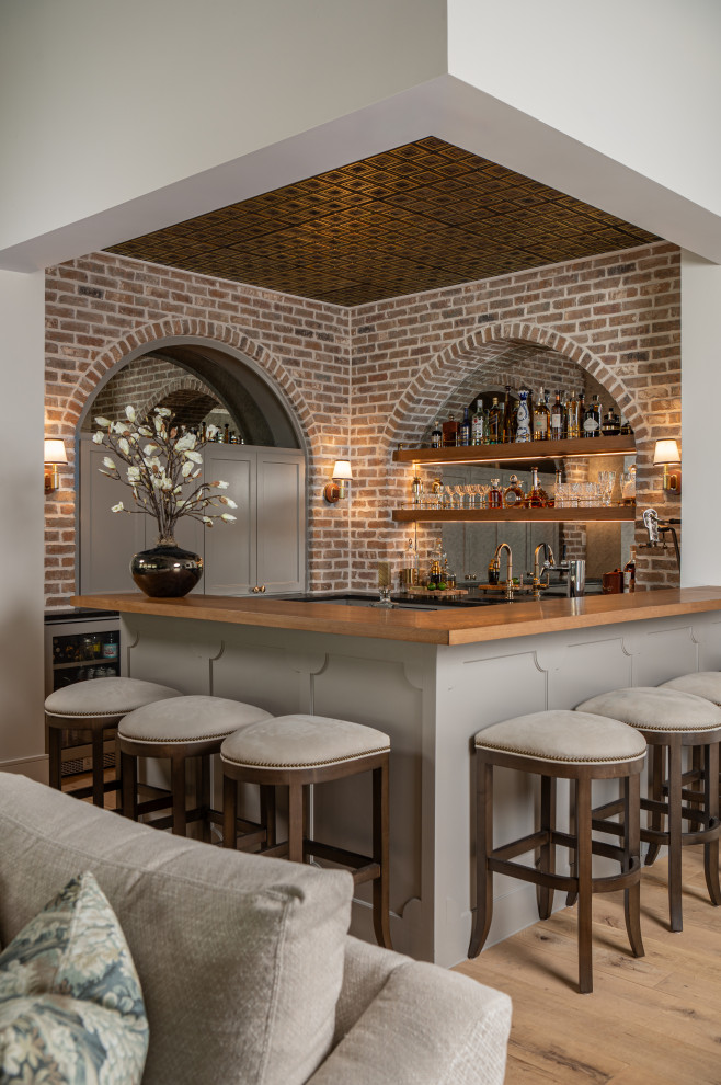 Example of a mid-sized cottage u-shaped light wood floor and beige floor wet bar design in Houston with shaker cabinets, gray cabinets, wood countertops, mirror backsplash and brown countertops