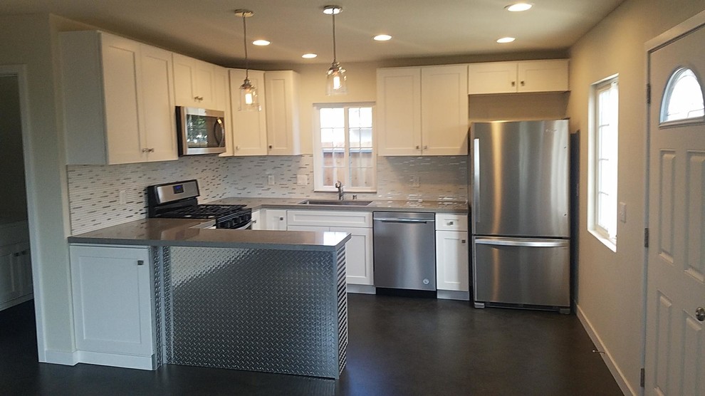 This is an example of a small industrial u-shaped open plan kitchen in San Diego with an undermount sink, shaker cabinets, white cabinets, quartz benchtops, white splashback, porcelain splashback, stainless steel appliances, concrete floors, a peninsula, grey floor and grey benchtop.