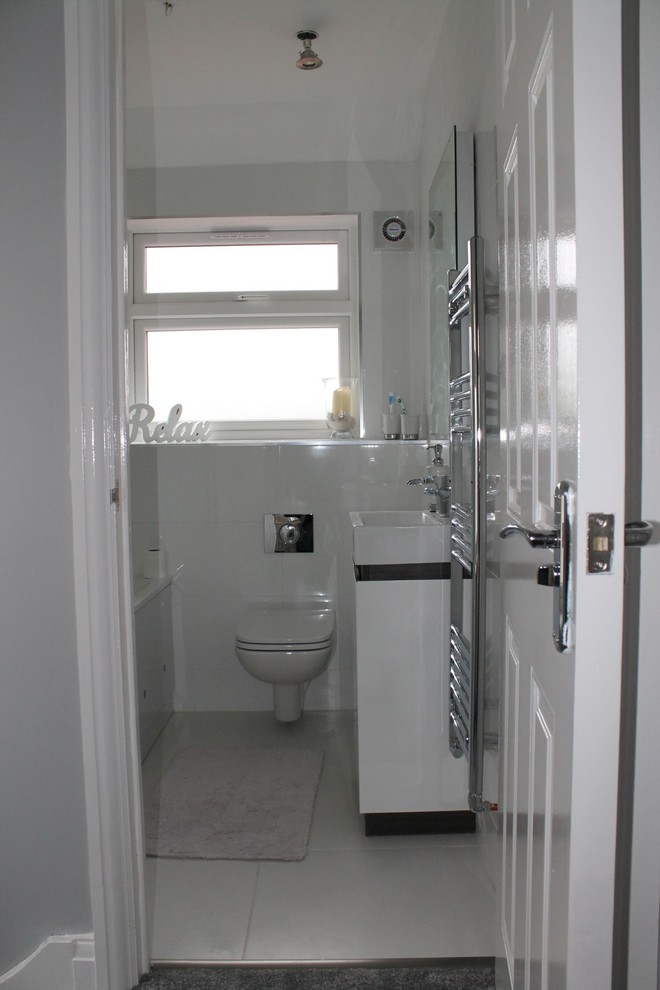Photo of a small modern kids bathroom in London with flat-panel cabinets, white cabinets, a drop-in tub, a shower/bathtub combo, a one-piece toilet, multi-coloured tile, ceramic tile, white walls, ceramic floors and a console sink.