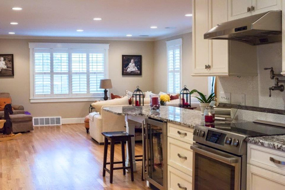Inspiration for a mid-sized transitional single-wall light wood floor eat-in kitchen remodel with recessed-panel cabinets, beige cabinets, granite countertops, white backsplash, matchstick tile backsplash, stainless steel appliances, a peninsula and a farmhouse sink
