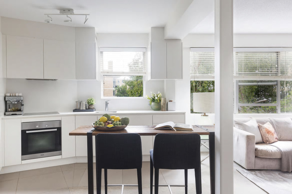 Contemporary single-wall open plan kitchen in Sydney with an undermount sink, flat-panel cabinets, white cabinets, white splashback, stainless steel appliances, with island and beige floor.