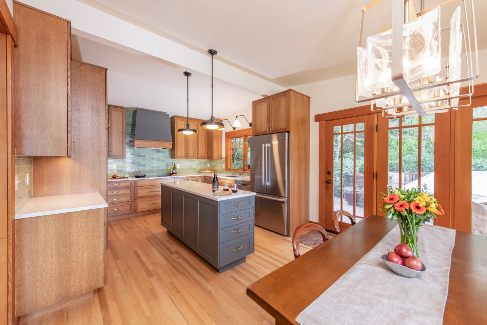 Example of a mid-sized transitional u-shaped medium tone wood floor, brown floor and vaulted ceiling eat-in kitchen design in Seattle with a double-bowl sink, recessed-panel cabinets, light wood cabinets, quartz countertops, blue backsplash, ceramic backsplash, stainless steel appliances, an island and white countertops