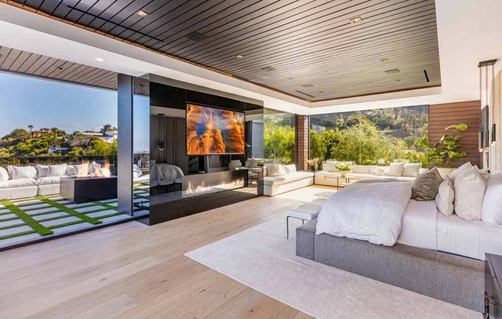 Geräumiges Modernes Hauptschlafzimmer mit Kamin, Kaminumrandung aus Stein, beigem Boden und eingelassener Decke in Los Angeles