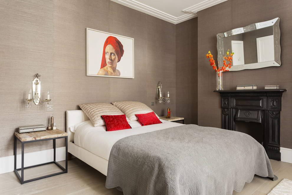 Photo of a transitional bedroom in London with light hardwood floors, a standard fireplace and brown walls.