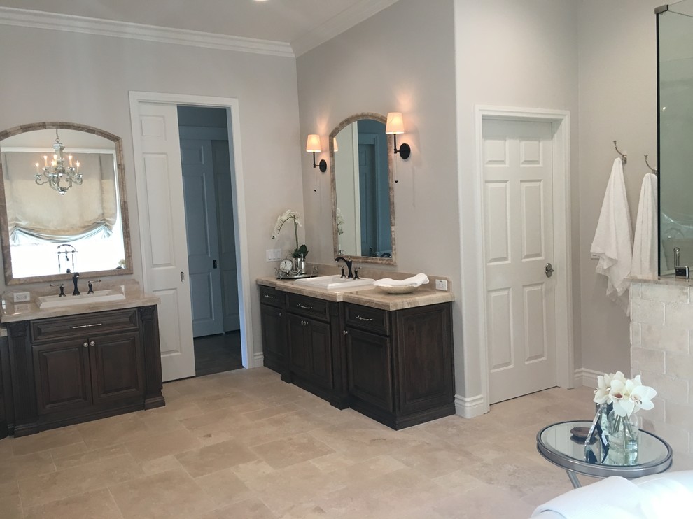 Inspiration for a large traditional master bathroom in Los Angeles with raised-panel cabinets, medium wood cabinets, a freestanding tub, a corner shower, a two-piece toilet, beige tile, travertine, beige walls, travertine floors, a drop-in sink, marble benchtops, beige floor and a hinged shower door.
