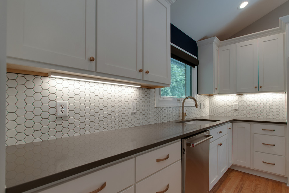 This is an example of a mid-sized midcentury u-shaped kitchen in Nashville with an undermount sink, shaker cabinets, white cabinets, quartzite benchtops, white splashback, ceramic splashback, stainless steel appliances, light hardwood floors, with island and brown floor.