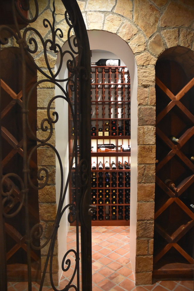 Réalisation d'une cave à vin vintage de taille moyenne avec tomettes au sol, un présentoir et un sol orange.