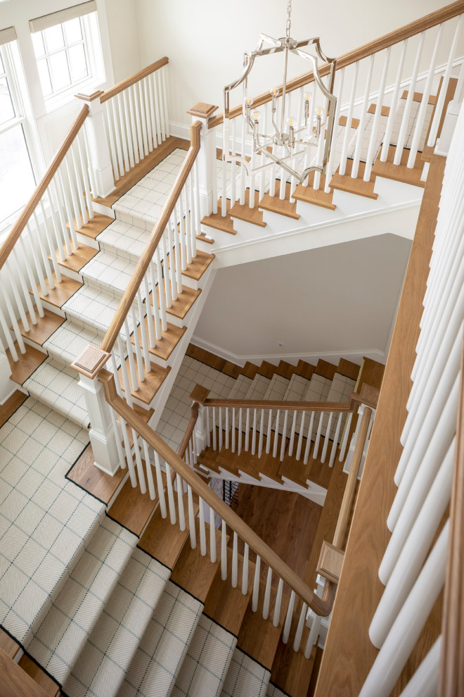 На фото: большая изогнутая лестница в классическом стиле с деревянными ступенями, крашенными деревянными подступенками и деревянными перилами с