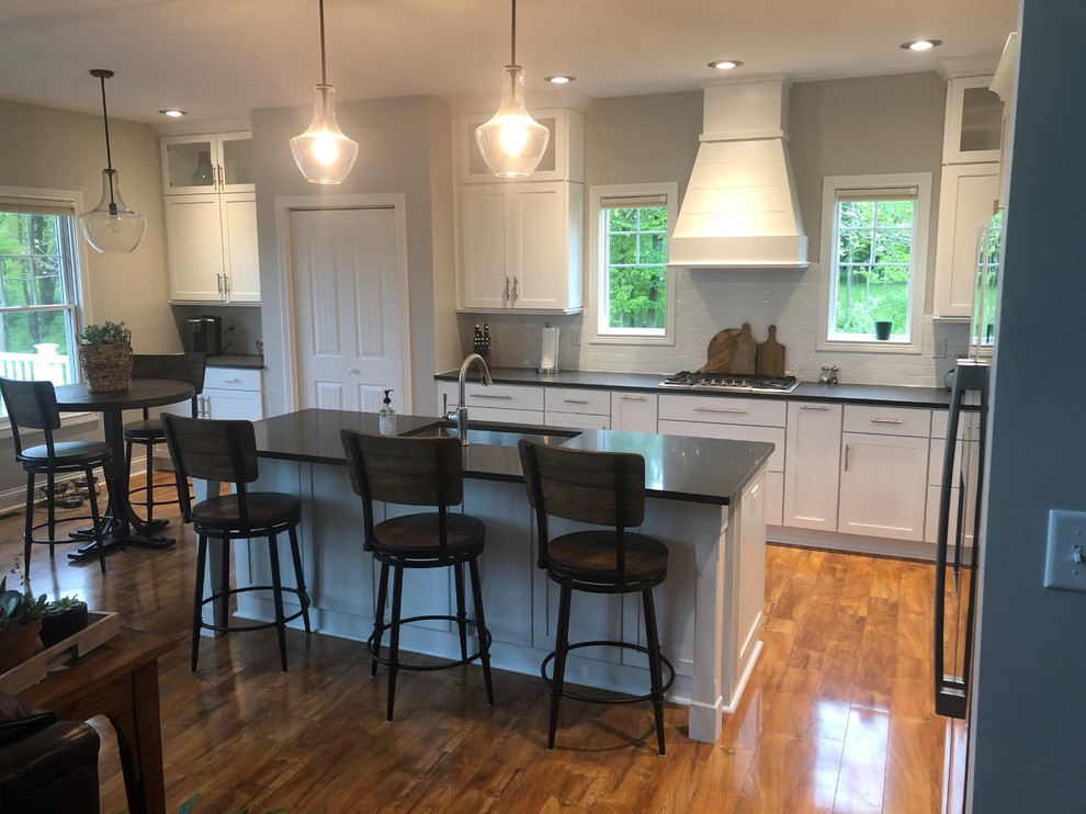 Inspiration for a laminate floor and brown floor kitchen remodel with a single-bowl sink, shaker cabinets, white cabinets, quartzite countertops, white backsplash, subway tile backsplash, stainless steel appliances, an island and gray countertops