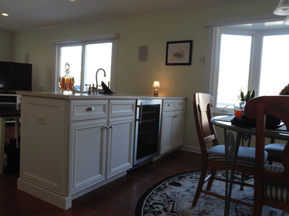 Example of a large transitional u-shaped medium tone wood floor and brown floor eat-in kitchen design with a farmhouse sink, flat-panel cabinets, white cabinets, quartz countertops, beige backsplash, travertine backsplash, stainless steel appliances and beige countertops