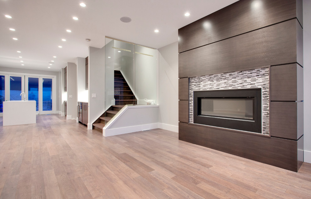 Photo of a small modern loft-style living room in Calgary with grey walls, medium hardwood floors, a standard fireplace, a tile fireplace surround and a freestanding tv.