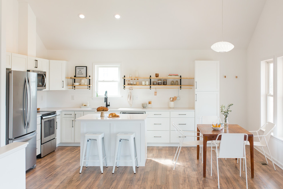 Example of a transitional l-shaped medium tone wood floor and brown floor eat-in kitchen design with an undermount sink, shaker cabinets, white cabinets, stainless steel appliances, an island and white countertops
