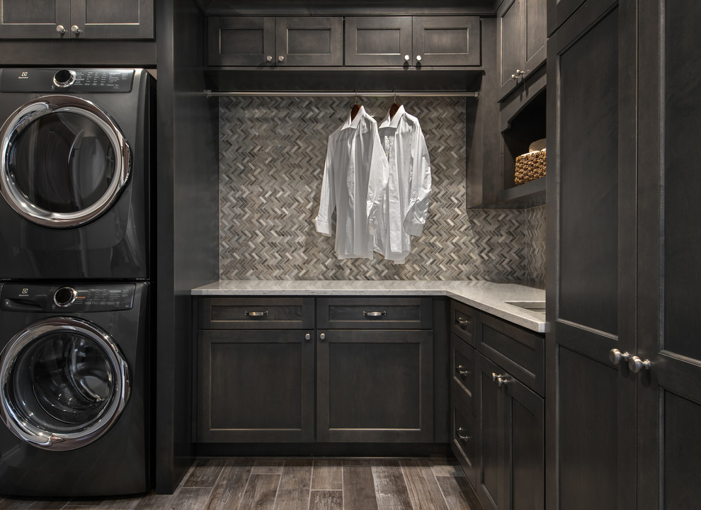 This is an example of a mid-sized transitional l-shaped laundry room in Detroit with an undermount sink, flat-panel cabinets, dark wood cabinets, quartz benchtops, beige walls, porcelain floors and a stacked washer and dryer.