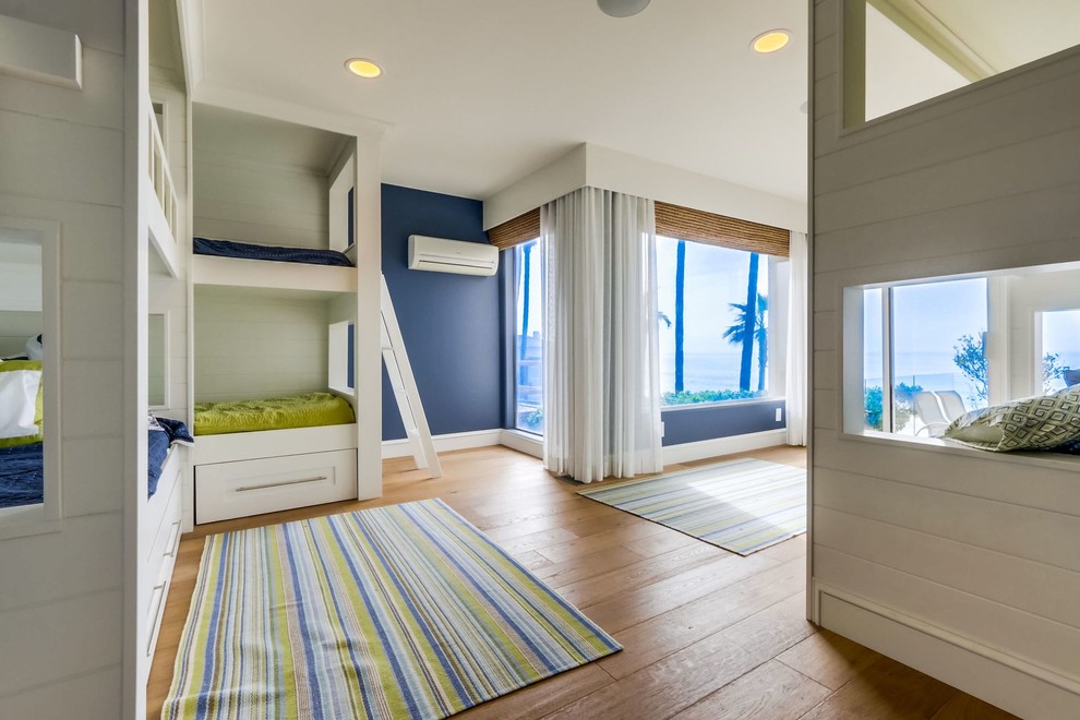Large beach style gender-neutral kids' bedroom in Orange County with blue walls, medium hardwood floors and brown floor for kids 4-10 years old.