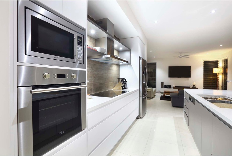 This is an example of a mid-sized contemporary galley open plan kitchen in Sunshine Coast with an undermount sink, white cabinets, quartz benchtops, brown splashback, ceramic splashback, stainless steel appliances, ceramic floors and with island.