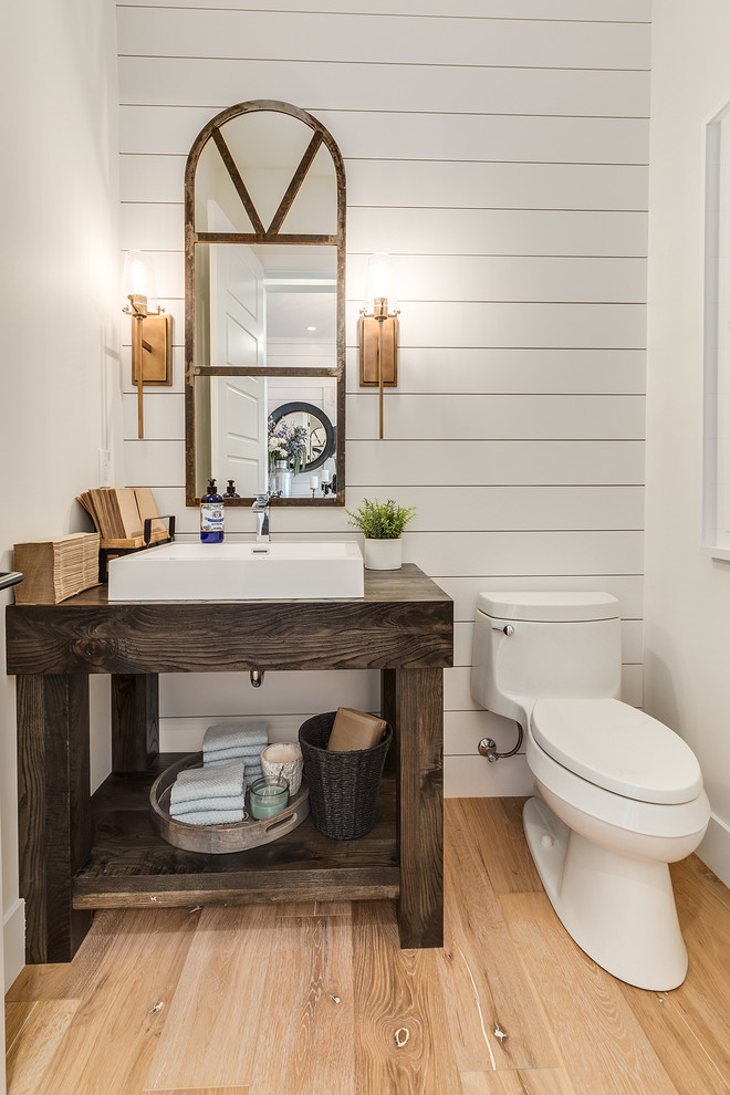 Large country powder room in Calgary with furniture-like cabinets, dark wood cabinets, a one-piece toilet, white walls, light hardwood floors, a vessel sink, wood benchtops, beige floor and brown benchtops.