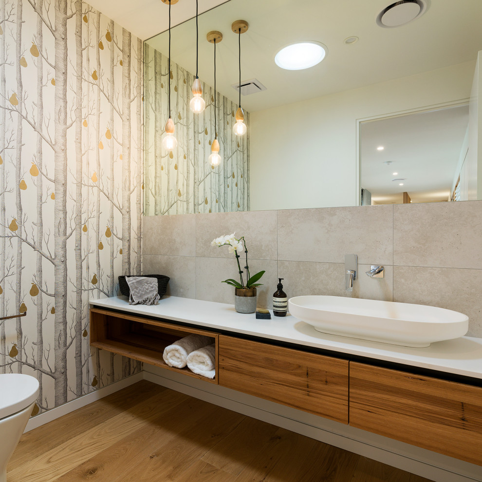 Mid-sized contemporary bathroom in Other with flat-panel cabinets, medium wood cabinets, gray tile, porcelain tile, multi-coloured walls, medium hardwood floors, a vessel sink, brown floor and white benchtops.