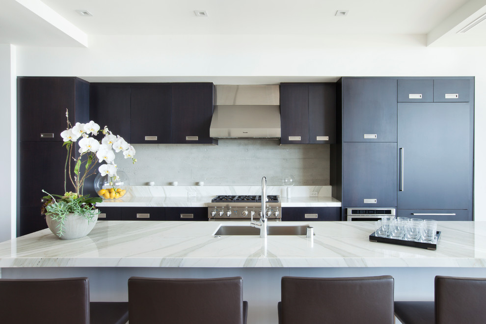 Photo of a mid-sized contemporary single-wall open plan kitchen in Los Angeles with an undermount sink, flat-panel cabinets, dark wood cabinets, marble benchtops, white splashback, stone slab splashback, panelled appliances, light hardwood floors and with island.