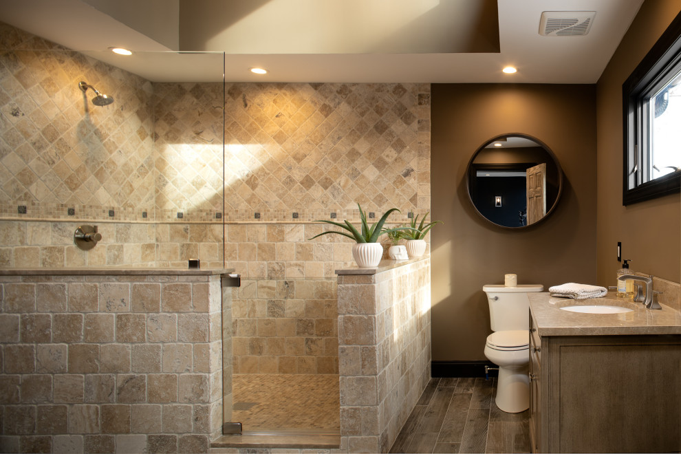 Photo of a large contemporary 3/4 bathroom in New York with medium wood cabinets, a two-piece toilet, travertine, brown walls, wood-look tile, an undermount sink, grey floor, a hinged shower door, a single vanity and a freestanding vanity.