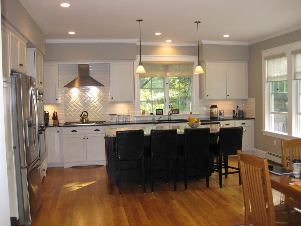 Inspiration for a transitional l-shaped medium tone wood floor eat-in kitchen remodel in Boston with an undermount sink, shaker cabinets, white cabinets, granite countertops, white backsplash, ceramic backsplash, stainless steel appliances, an island and black countertops