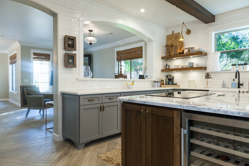 Large transitional l-shaped porcelain tile and brown floor eat-in kitchen photo in Phoenix with a farmhouse sink, shaker cabinets, gray cabinets, quartz countertops, white backsplash, glass sheet backsplash, stainless steel appliances, an island and white countertops
