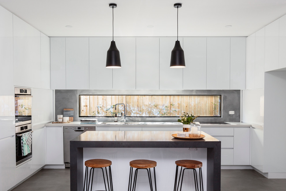 Inspiration for a mid-sized contemporary u-shaped eat-in kitchen in Melbourne with a drop-in sink, flat-panel cabinets, white cabinets, quartz benchtops, stainless steel appliances, concrete floors and with island.