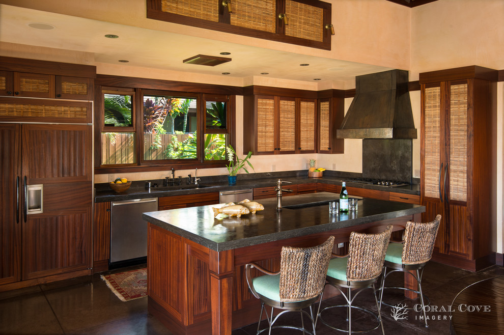 This is an example of a mid-sized tropical l-shaped open plan kitchen in Hawaii with an integrated sink, recessed-panel cabinets, medium wood cabinets, granite benchtops, black splashback, stone slab splashback, stainless steel appliances, concrete floors and with island.