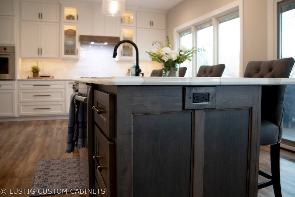 Inspiration for a large transitional l-shaped laminate floor and brown floor open concept kitchen remodel with an undermount sink, flat-panel cabinets, white cabinets, quartz countertops, white backsplash, ceramic backsplash, stainless steel appliances, an island and white countertops