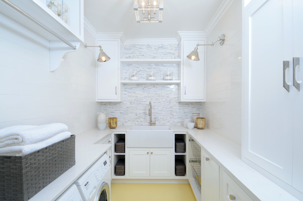 This is an example of a mid-sized transitional u-shaped dedicated laundry room in Los Angeles with a farmhouse sink, shaker cabinets, white cabinets, solid surface benchtops, white walls, painted wood floors and a side-by-side washer and dryer.