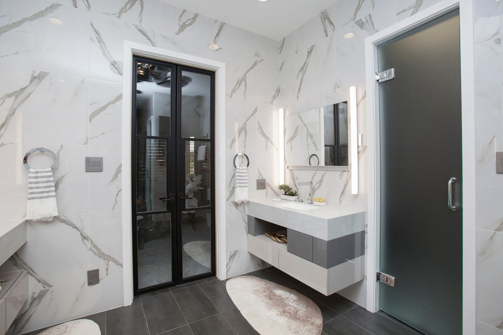 Photo of a large contemporary master bathroom in Dallas with flat-panel cabinets, white cabinets, a hot tub, a one-piece toilet, gray tile, porcelain tile, a drop-in sink, limestone benchtops, an alcove shower and white walls.