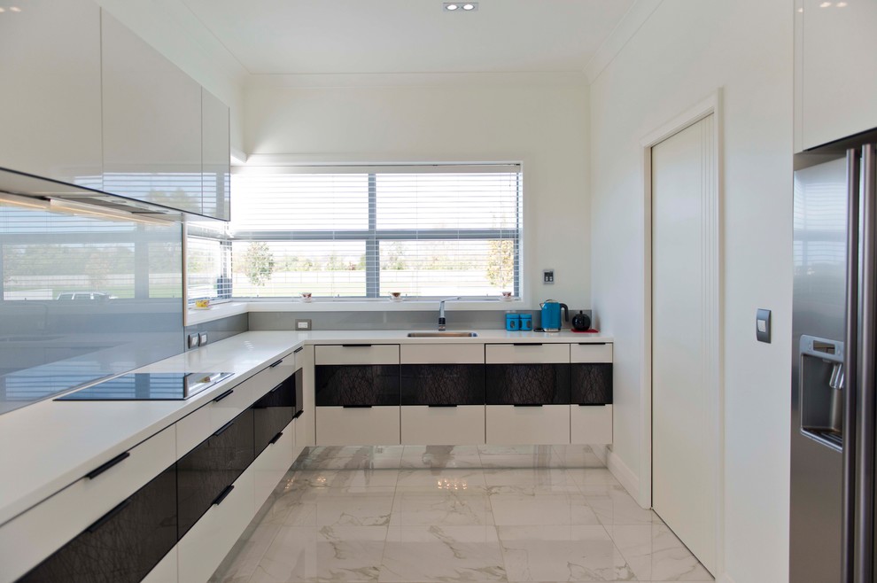 Large modern l-shaped kitchen pantry in Christchurch with an undermount sink, flat-panel cabinets, white cabinets, solid surface benchtops, yellow splashback, glass sheet splashback, stainless steel appliances, ceramic floors, multiple islands and white floor.